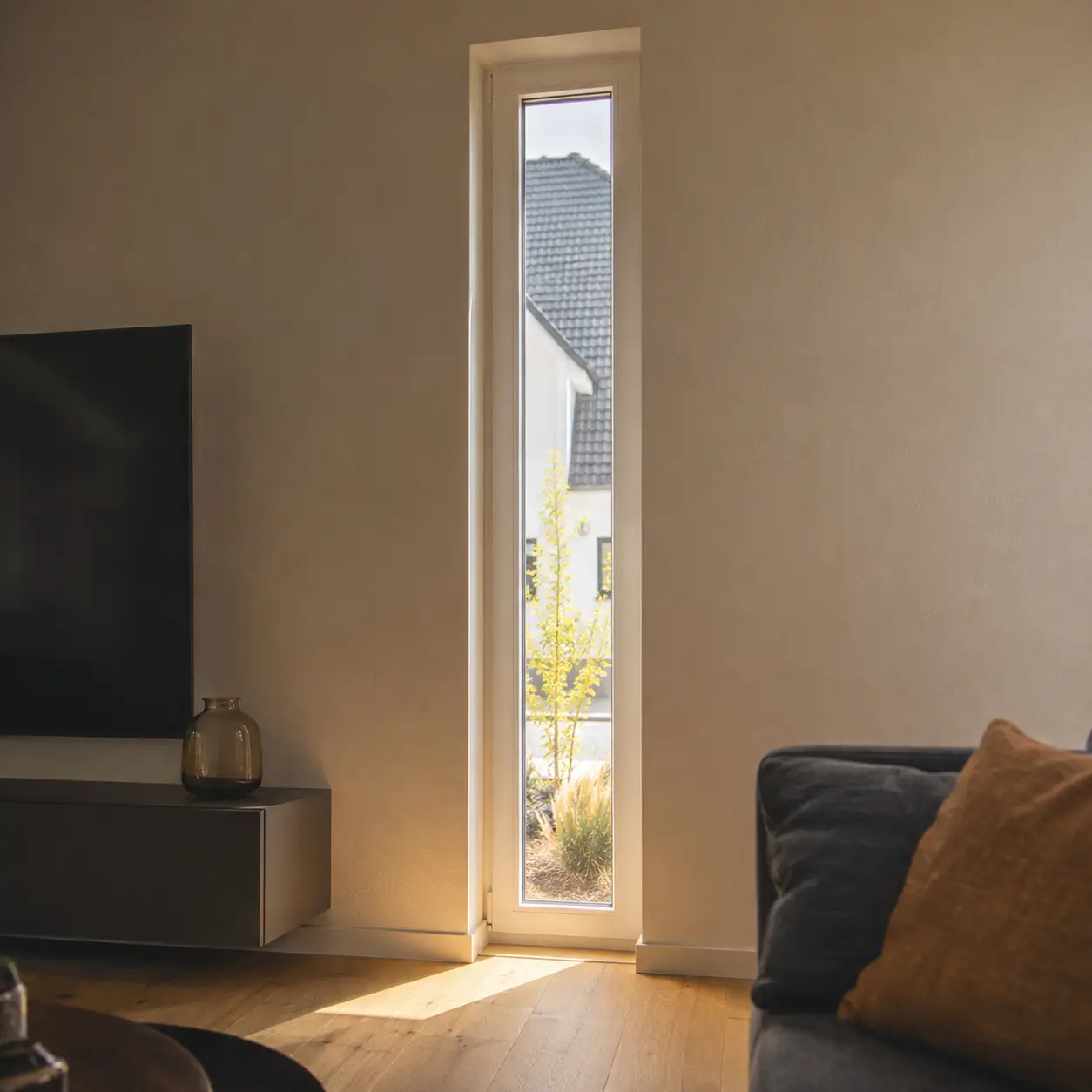Schmales hohes Fenster mit weißem Rahmen in einer modernen Wohnraumwand von ecowindow